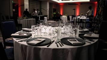 A dining area with round tables set for a formal meal, featuring white tablecloths, black plates, and silverware.