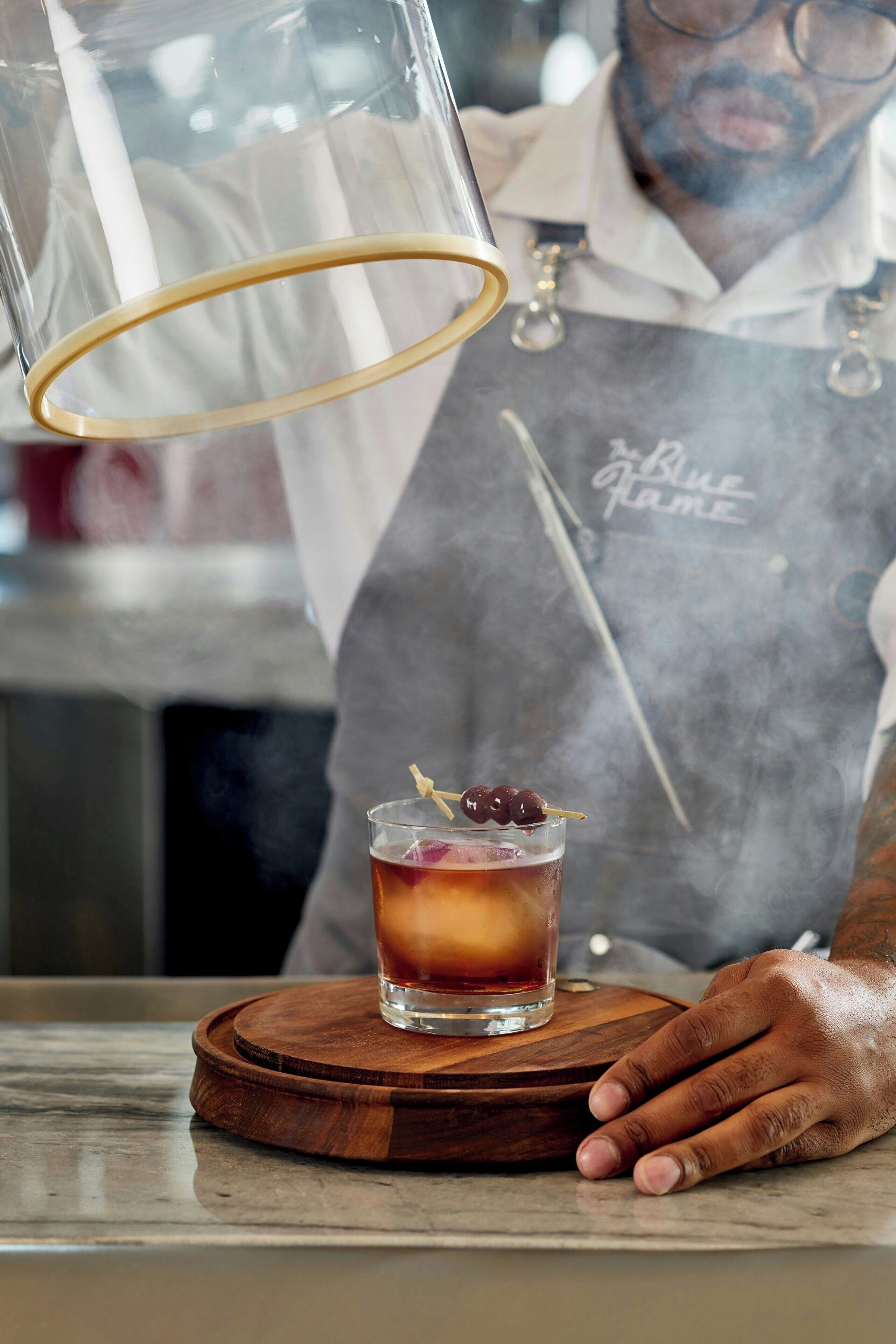 Un barman verse une boisson dans un verre posé sur un sous-verre en bois.