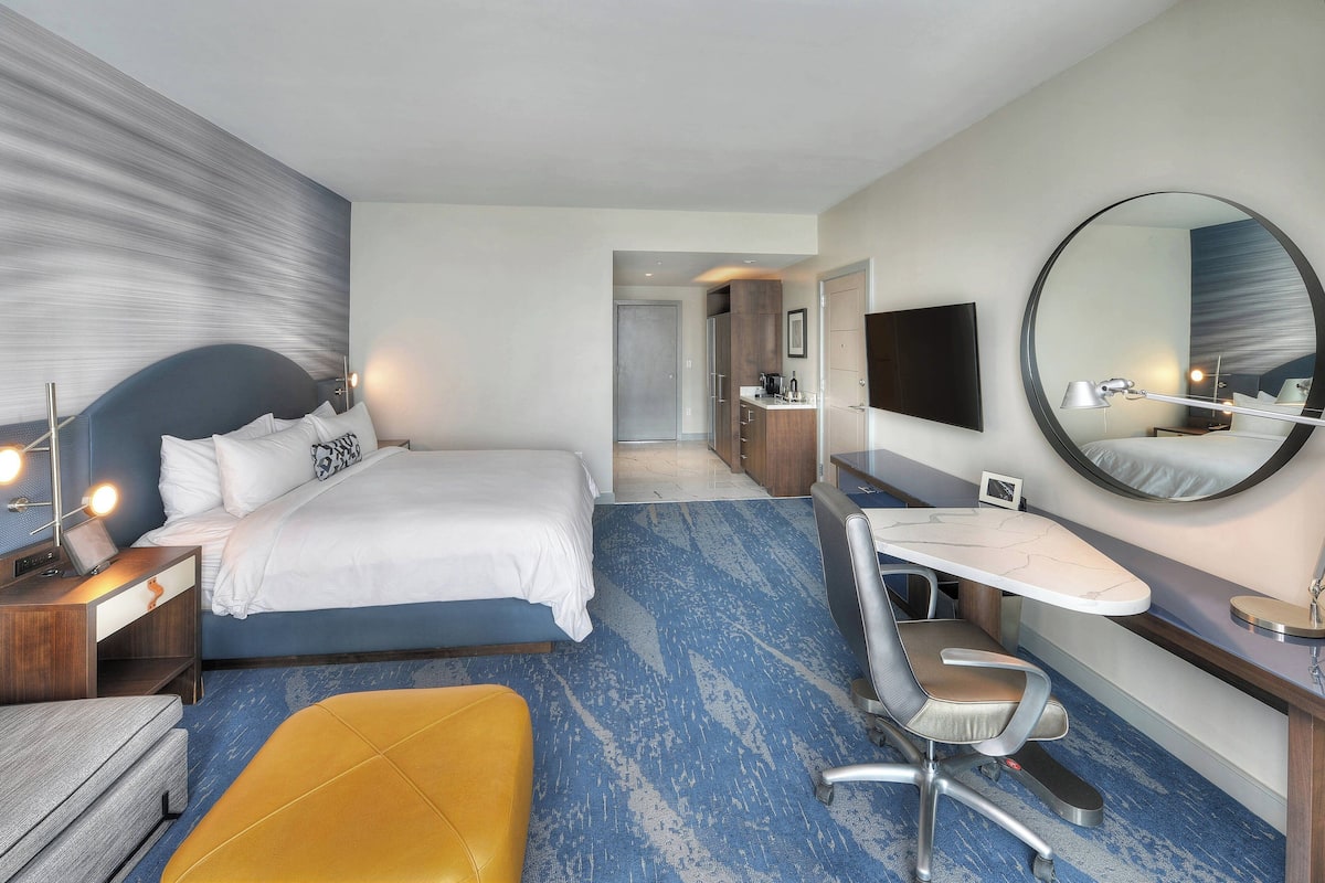 A hotel room with a bed, desk, chair, and a large mirror.