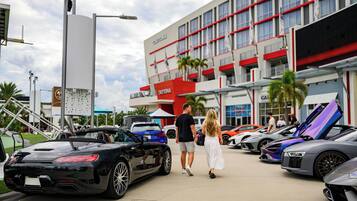 Ein Gebäude mit roter und weißer Fassade, mehreren Flaggen und einem Parkplatz mit Luxusautos.