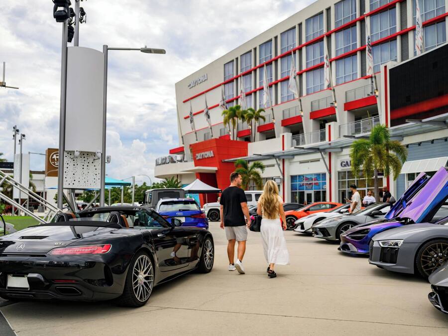 Ein Gebäude mit roter und weißer Fassade, mehreren Flaggen und einem Parkplatz mit Luxusautos.