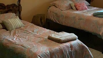 Dos camas individuales con colchas estampadas, una mesita de noche, una lámpara y un adorno de árbol en la pared.