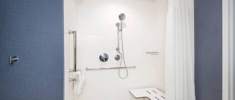 A shower with a handheld showerhead and a wall-mounted faucet, a towel rack, and a small white shelf.