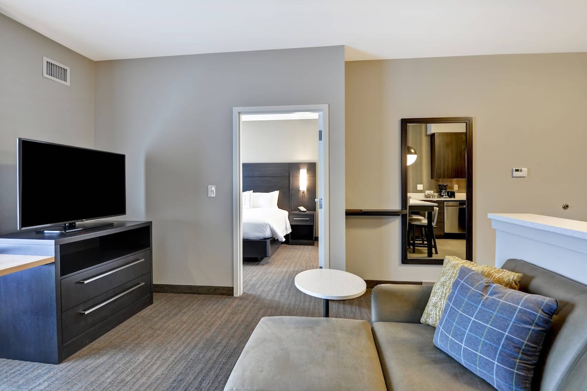 Une chambre d’hôtel équipée d’une télévision à écran plat, d’un canapé, d’une petite table ronde, d’un miroir et d’un lit avec une table de chevet.