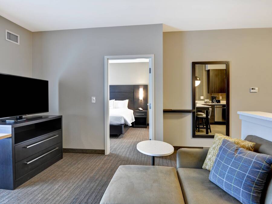 Une chambre d’hôtel équipée d’une télévision à écran plat, d’un canapé, d’une petite table ronde, d’un miroir et d’un lit avec une table de chevet.