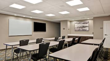 A conference room with tables, chairs, a projector screen, and a large abstract painting on the wall.