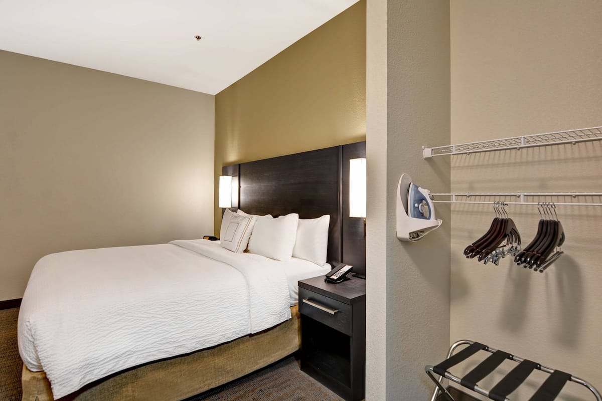 Une chambre d’hôtel avec un grand lit, une table de chevet, une lampe et un porte-chaussures.