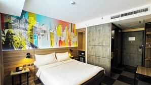 A modern hotel room with a large bed, a desk, and a chair. There is a colorful abstract painting on the wall and a large safe in the corner. - ibis Styles Bekasi Jatibening (Bekasi)