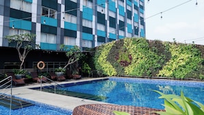 A swimming pool with lounge chairs and a hedge wall. - ibis Styles Bekasi Jatibening (Bekasi)