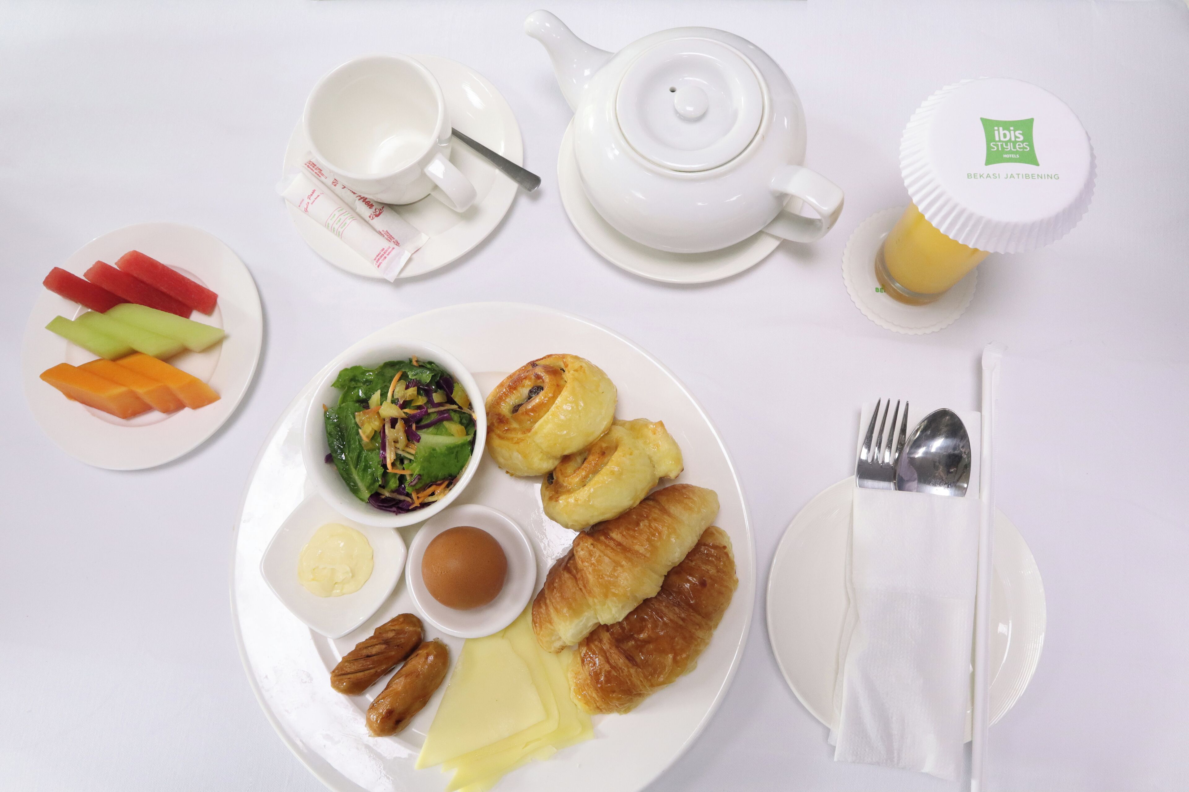 A table set with a variety of food items including croissants, a salad, and a plate of sliced vegetables.