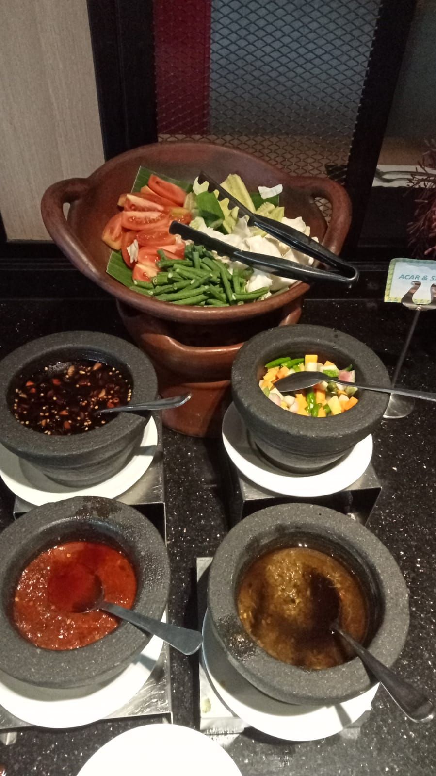 Un bufé con una variedad de platos, incluyendo una olla grande de vegetales, tazones con diferentes salsas y un letrero que dice 'ACAR & S'.