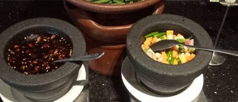 Un bufé con una variedad de platos, incluyendo una olla grande de vegetales, tazones con diferentes salsas y un letrero que dice 'ACAR & S'.