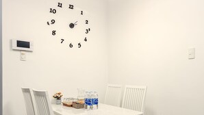 A dining area with a white table and chairs, a wall clock, and a ceiling light fixture.