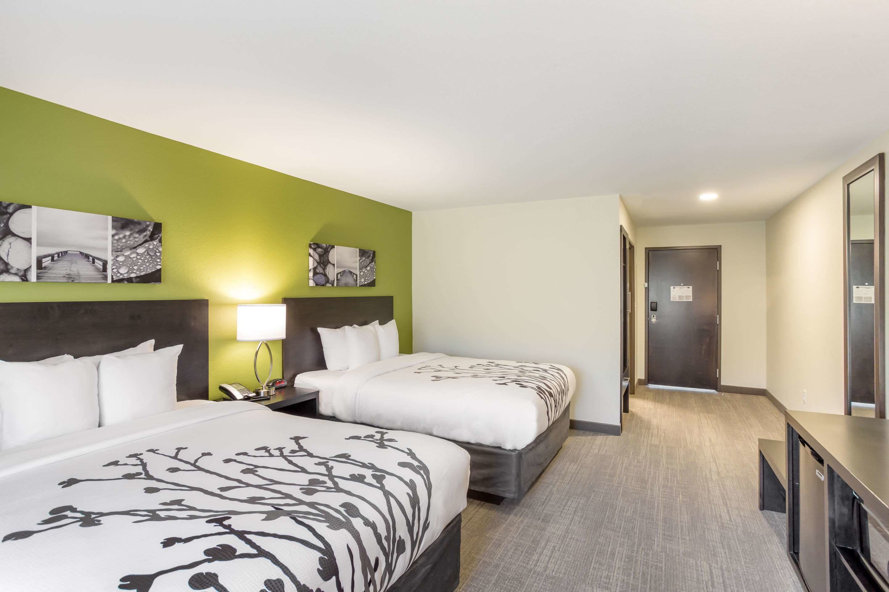 A hotel room with two beds, a nightstand, a lamp, and artwork on the wall.