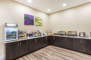 A breakfast bar with a refrigerator, coffee makers, and a variety of food items.