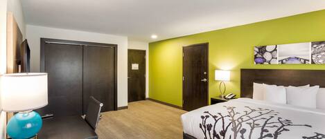 A hotel room with a bed, a desk with a lamp, a phone, and a painting on the wall.