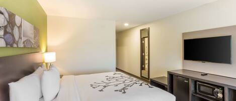 A hotel room with a bed, a flat-screen TV, a microwave, and a small cabinet.