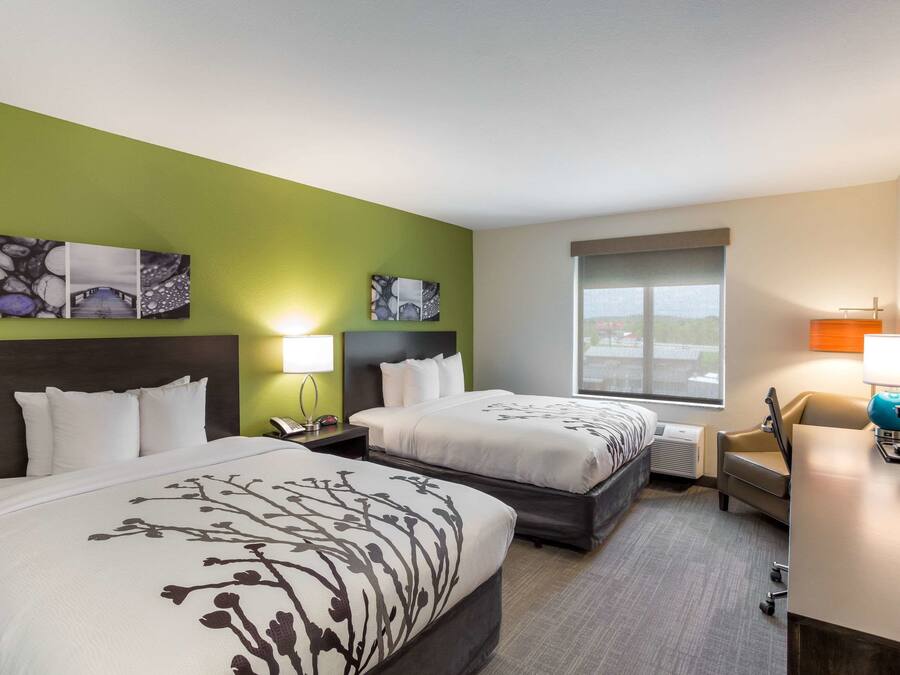 A hotel room with two beds, a desk, a chair, and artwork on the walls.