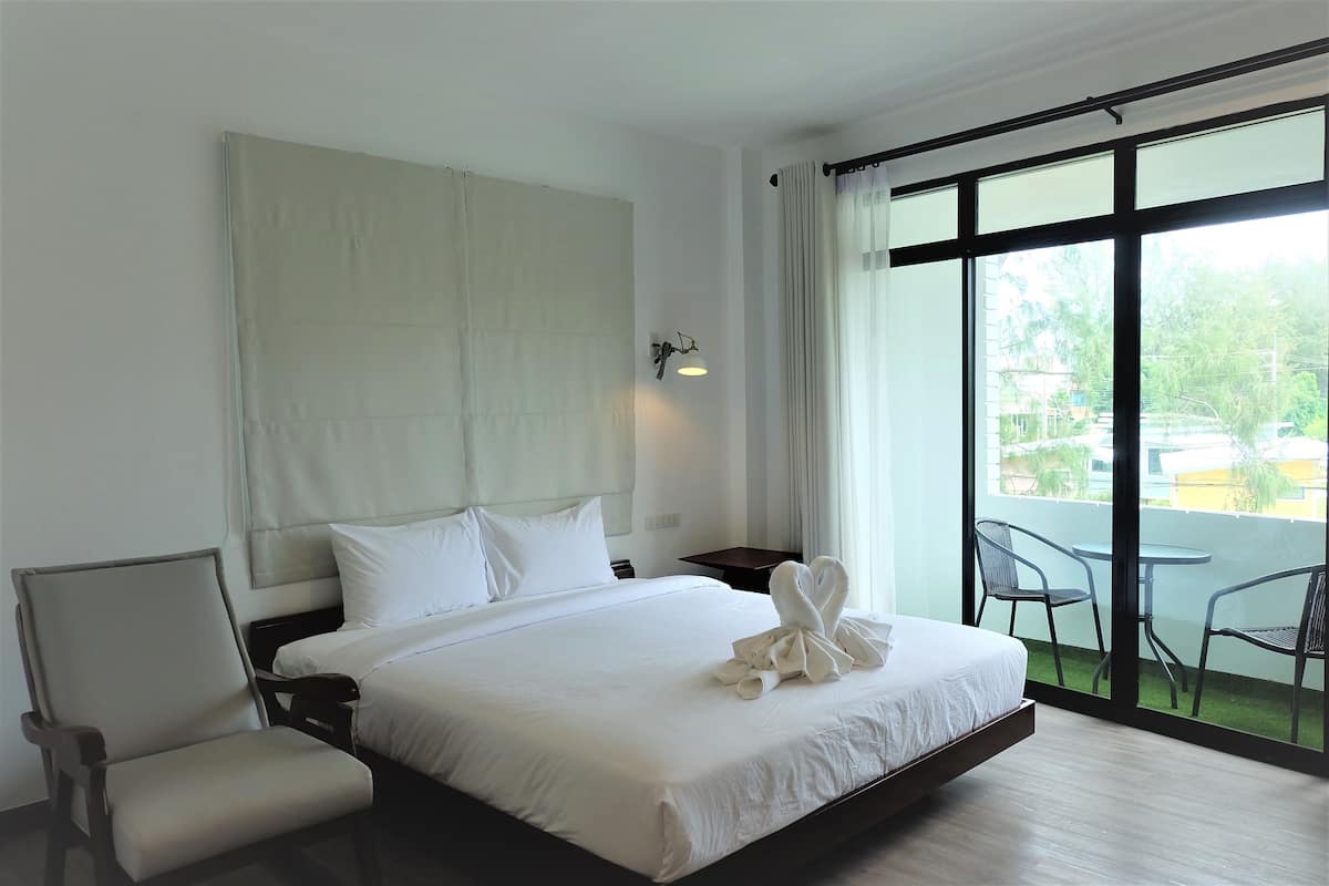 A hotel room with a large bed, a chair, a nightstand, and a view of the outdoors through a large window.