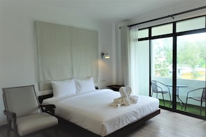 Une chambre d’hôtel avec un grand lit, une chaise, une table de chevet et une vue sur l’extérieur grâce à une grande fenêtre.