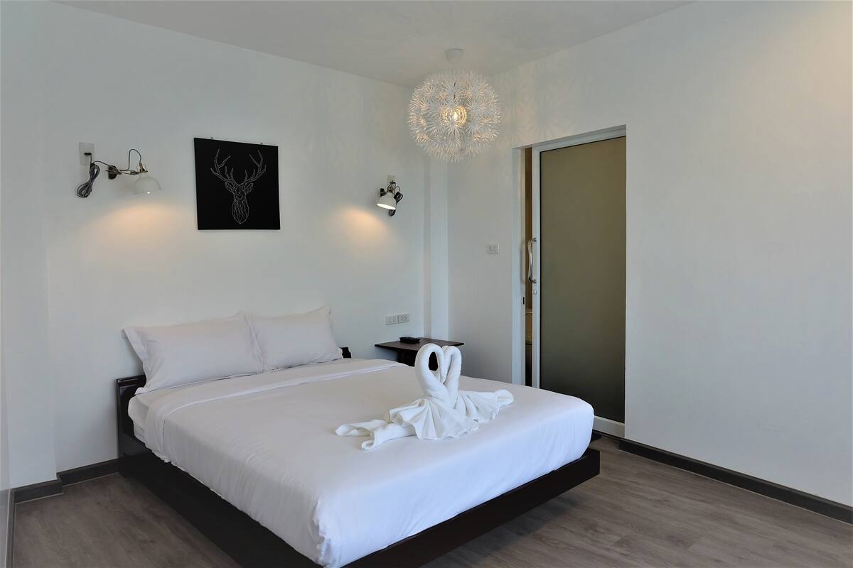 A hotel room with a bed, a wall-mounted light, a framed deer head artwork, and a decorative ceiling light.