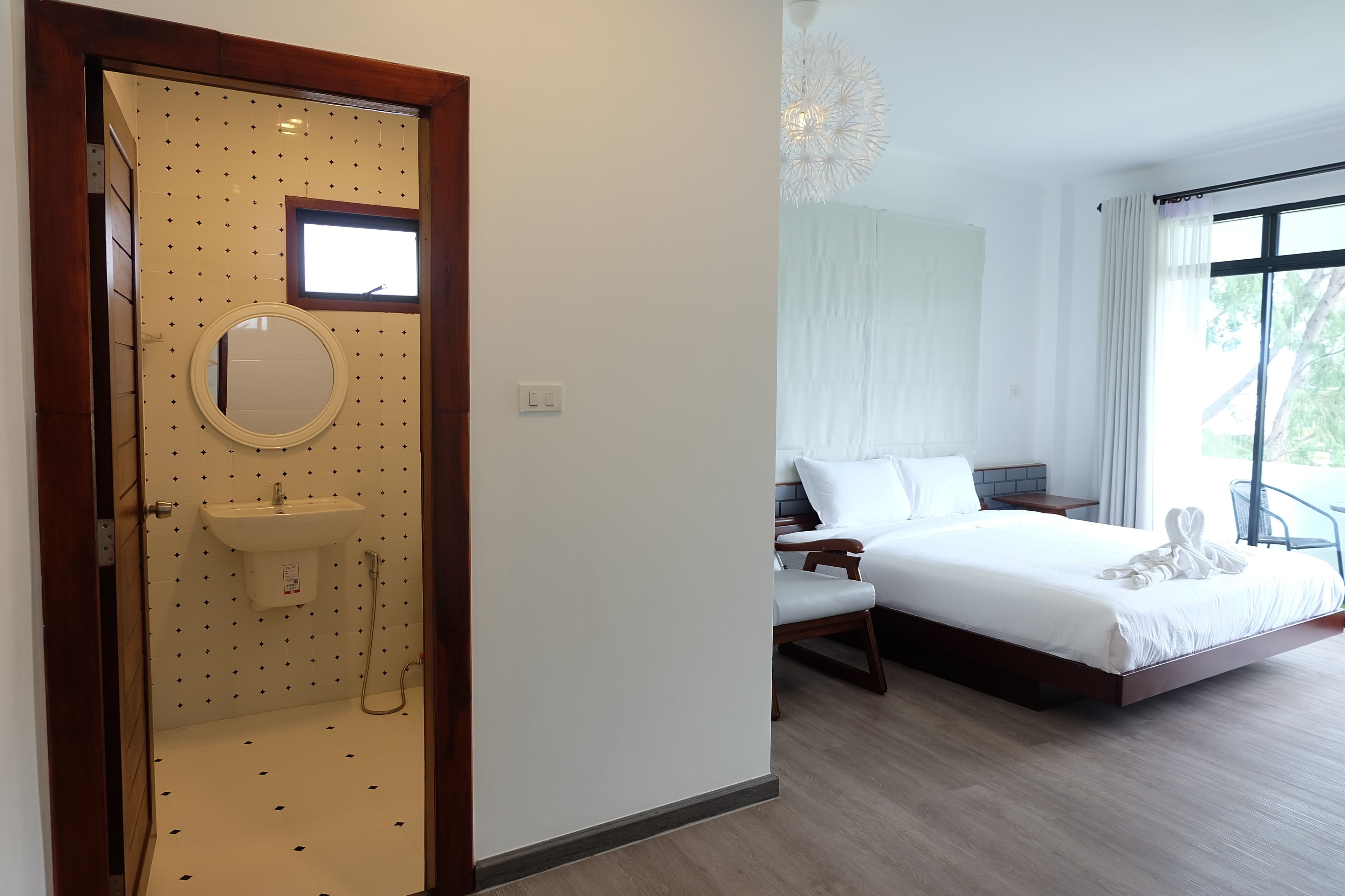 Une chambre d’hôtel comprenant un lit, une table de chevet, une chaise, une fenêtre avec des rideaux et une salle de bain avec un lavabo et un miroir.