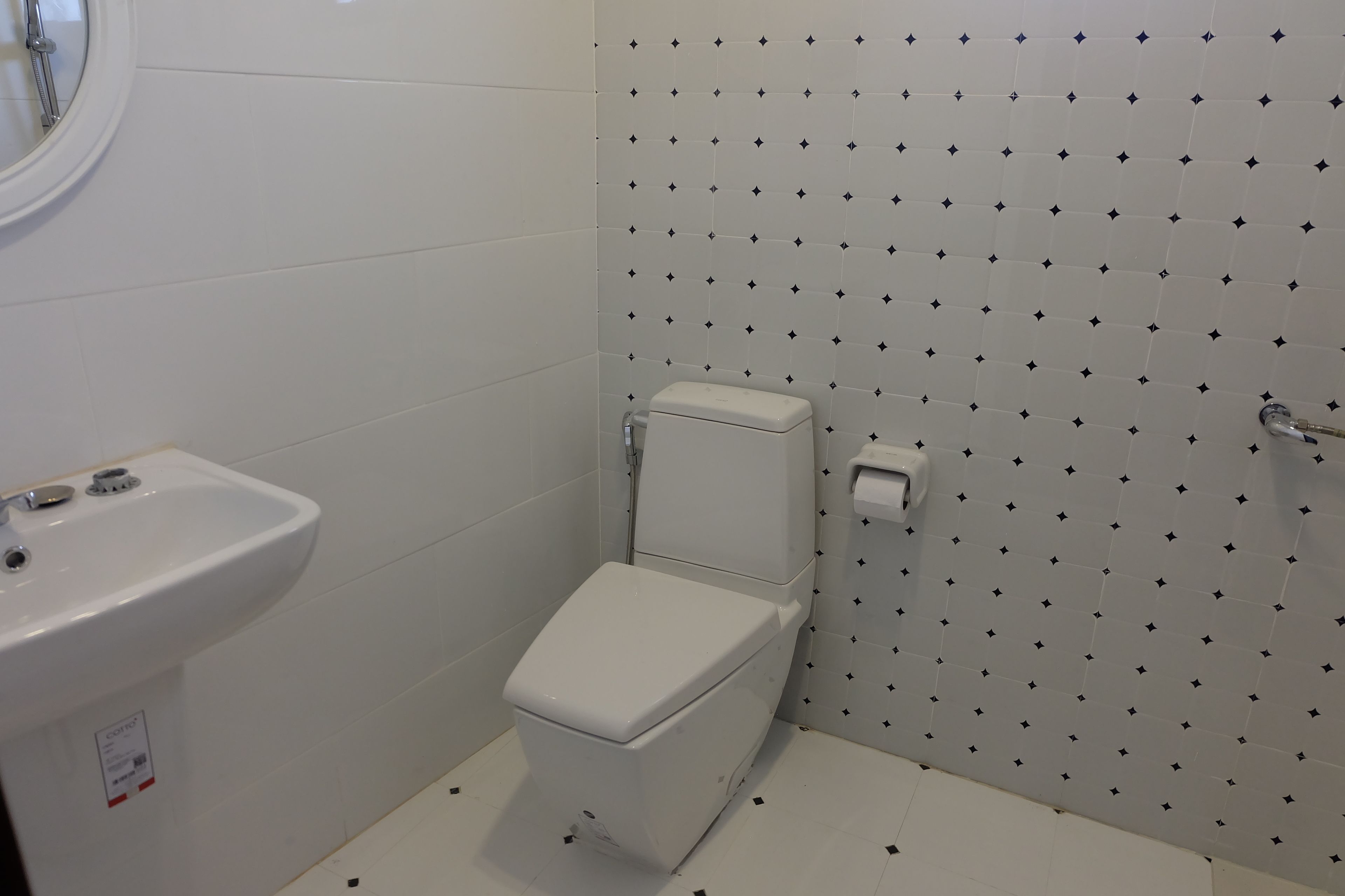 A small bathroom with a toilet, a sink, and a tiled wall with a diamond pattern.