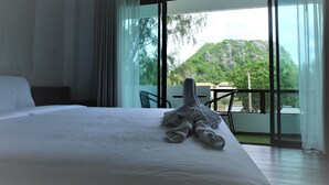 A hotel room with a large bed, a balcony with a table and chairs, and a view of a mountainous landscape. - Rublom & Chomview Huahin Pranburi (Pranburi)