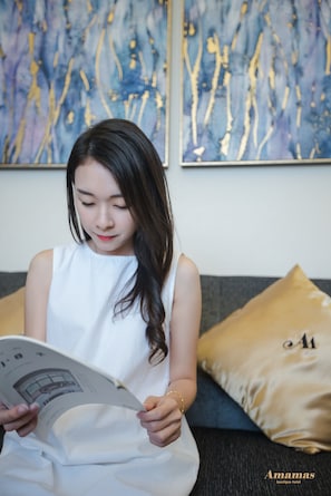 A person reading a magazine in a room with a modern abstract painting on the wall and a gold-colored pillow on the sofa. - Amamas Boutique Hotel Kuching (Kuching)