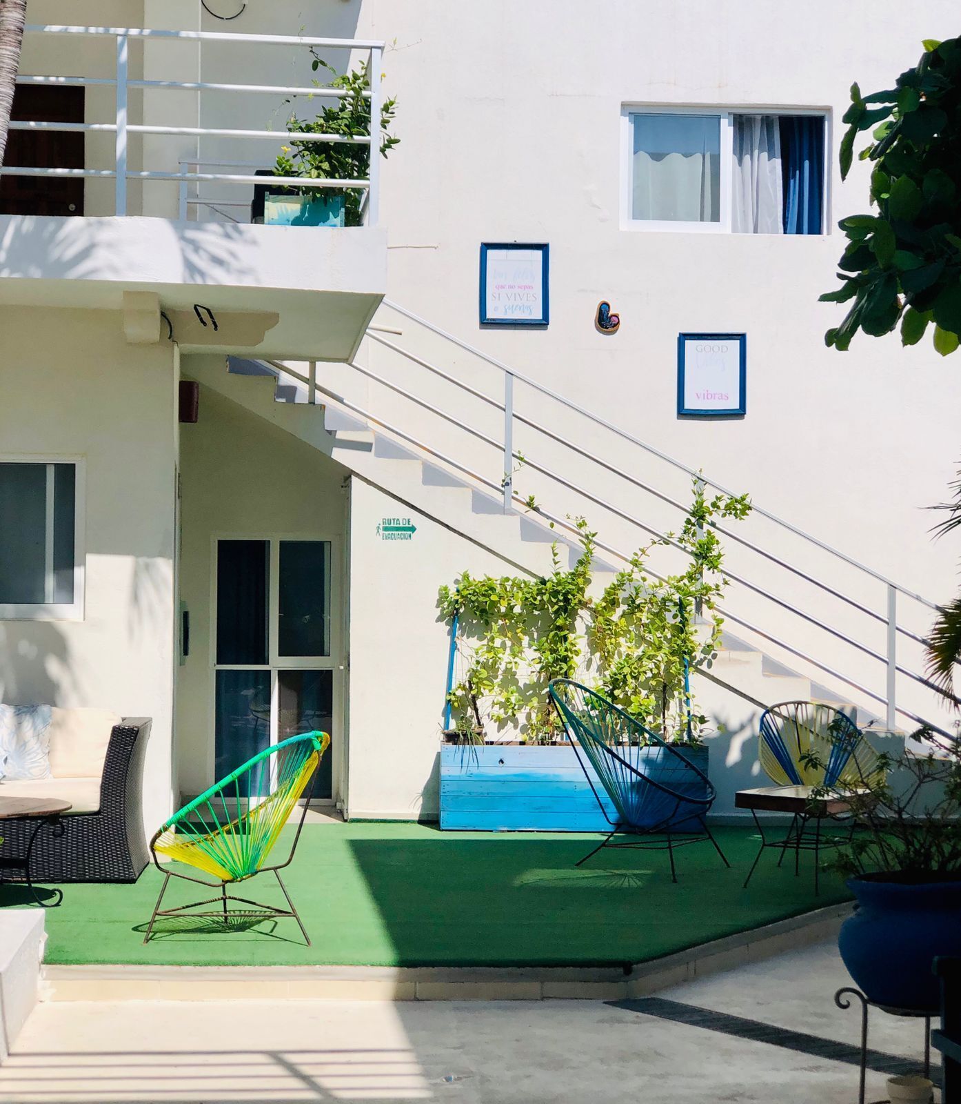 Un bâtiment doté d’un escalier menant à un étage supérieur, d’un espace extérieur verdoyant avec des chaises, et d’un panneau indiquant un itinéraire d’évacuation.