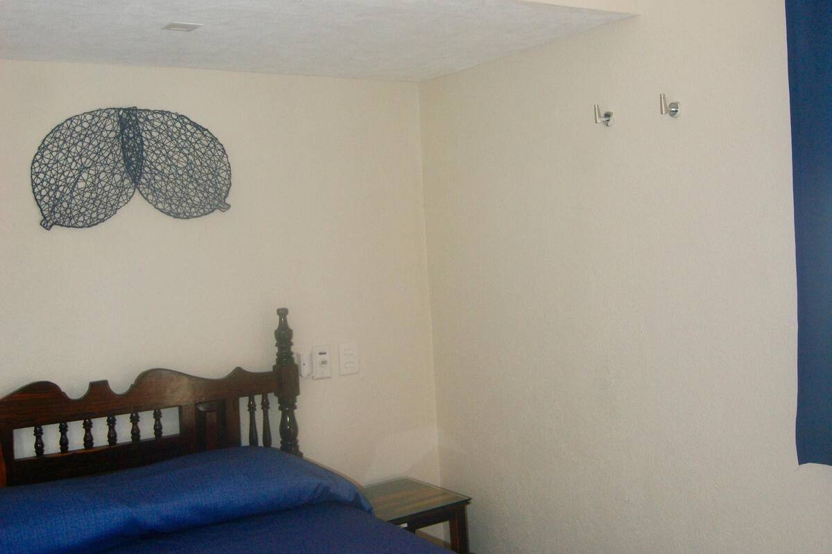 Un dormitorio con una cama, un ventilador de techo, una lámpara de pared y una puerta con cortina azul.