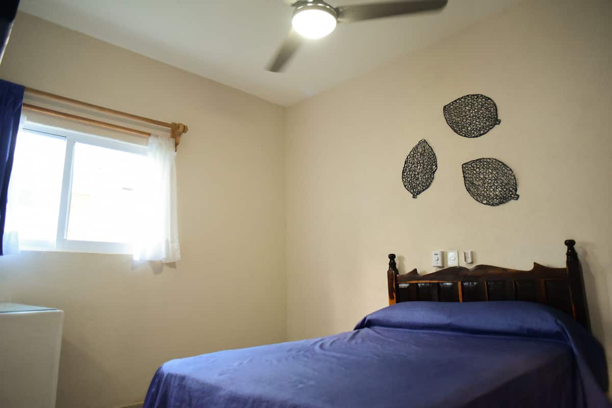 Un dormitorio con cama, ventilador de techo, ventana con cortinas y decoración en la pared.