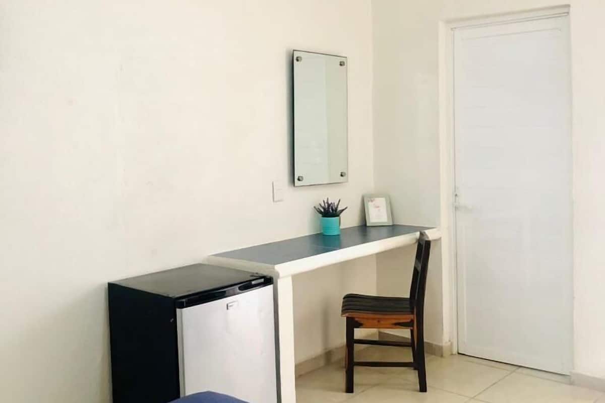 Un dormitorio con cama, escritorio, silla, ventilador de techo y puerta.