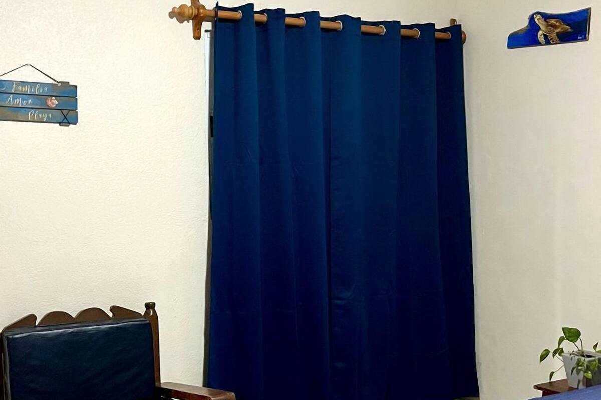 Una habitación con una cama, una silla, una cortina, un cartel en la pared y una planta pequeña.