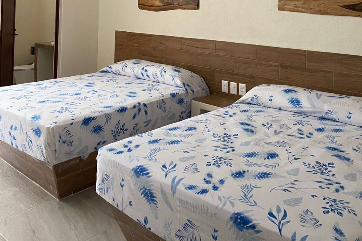 Una habitación con dos camas, cabeceros de madera, un ventilador de techo y una puerta que da a un baño.
