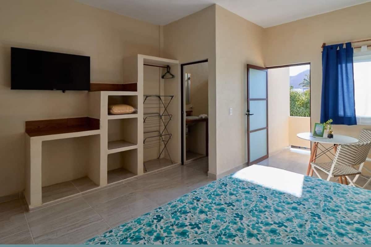 Una habitación con cama, televisión montada en la pared, armario, una pequeña mesa con sillas y vistas al exterior.