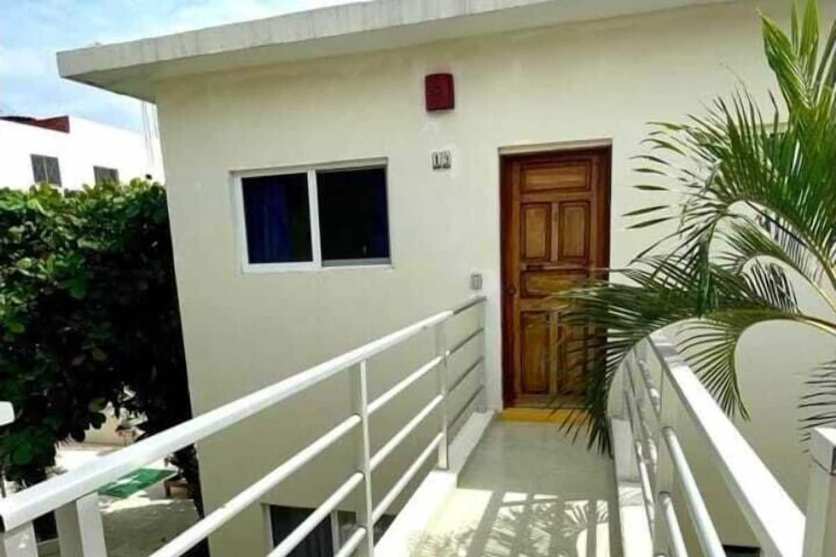 Un edificio blanco con puerta de madera, una ventana pequeña y barandal de metal.