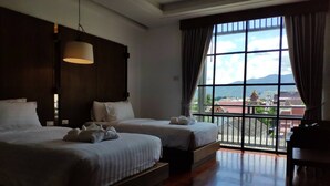 A hotel room with two beds, a large window with a view of buildings and mountains, and a hanging light fixture. - Anika Boutique Hotel (Chiang Mai)
