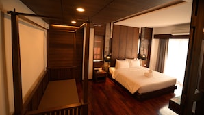 A hotel room with a wooden floor, a large bed with white linens, a nightstand with a lamp, and a window with curtains. - Anika Boutique Hotel (Chiang Mai)