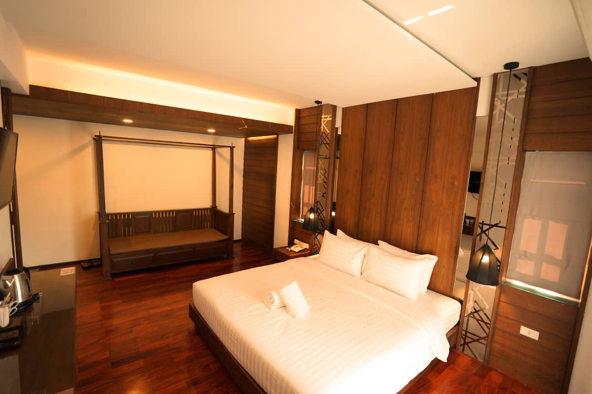 A hotel room with a large bed, a wooden bench, a desk with a kettle, and a wardrobe.
