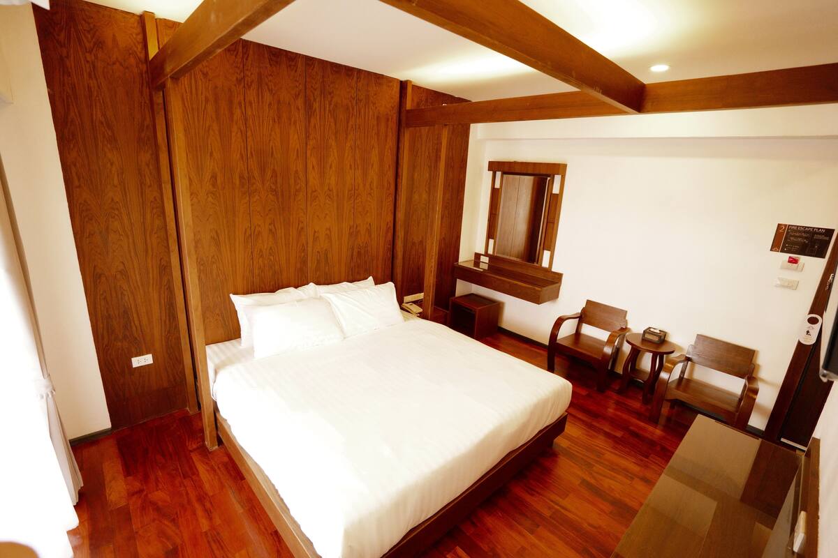 A hotel room with a wooden bed, a small desk, a chair, and a mirror.