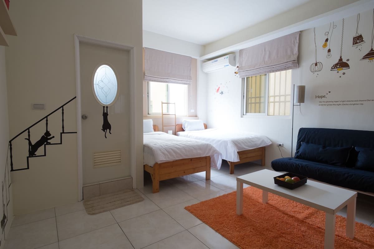 A room with two beds, a sofa, a table, and a staircase.