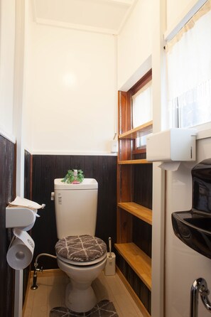 A compact bathroom with a toilet, a hand dryer, and a small shelf. - Sakura (Manazuru)