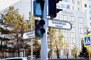 En trafikljus för fotgängare med riktningsanvisningar på ett främmande språk, en modern byggnad i bakgrunden och en skylt som visar en övergång för fotgängare.