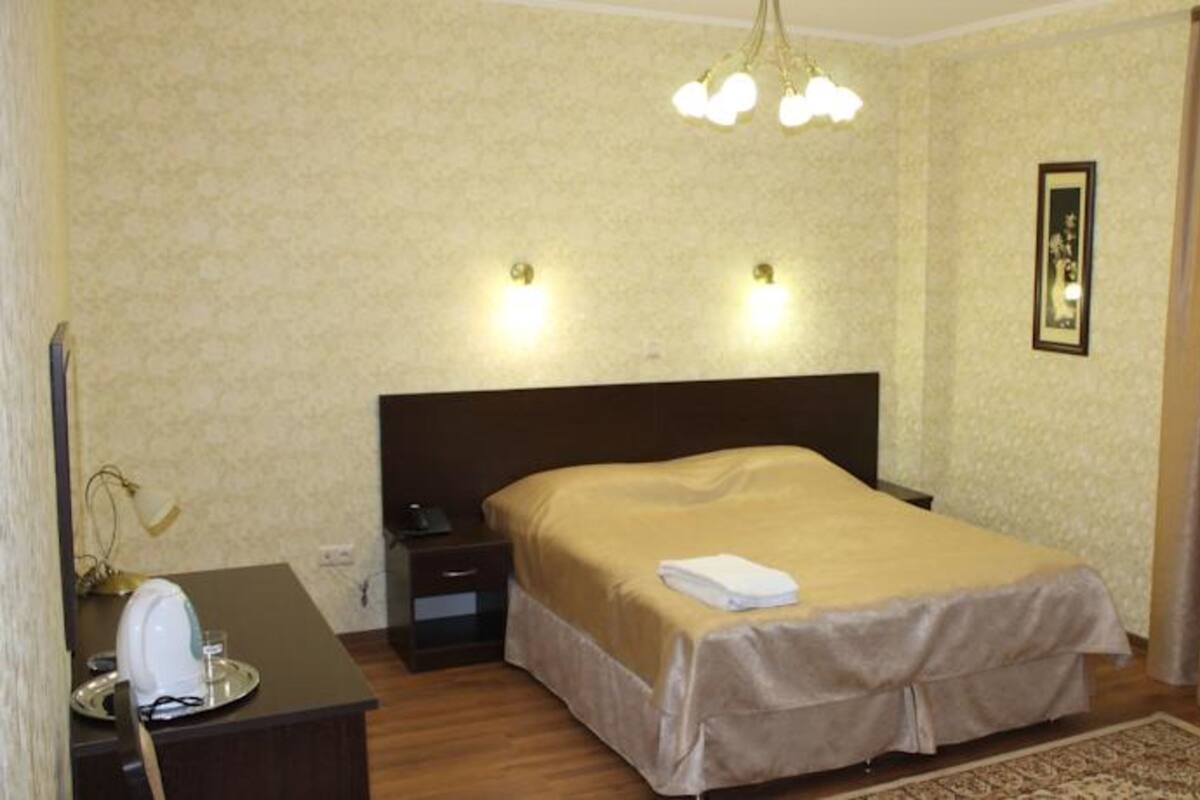 A hotel room with a bed, bedside table, lamp, and a framed picture on the wall.