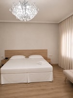 Una habitación de hotel con una cama grande, cabecero de madera, candelabro, mesita de noche con teléfono y ventana con cortinas.