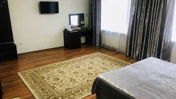 Habitación de hotel con una cama grande, un escritorio con computadora, un televisor y una ventana con cortinas.