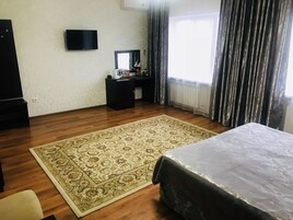 Habitación de hotel con una cama grande, un escritorio con computadora, un televisor y una ventana con cortinas.