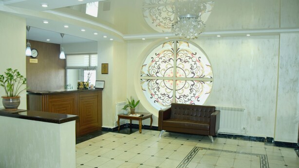 A hotel lobby with a reception desk, a sofa, a small table with a plant, and a decorative glass window. - Sultan Beibarys Hotel (Astana)