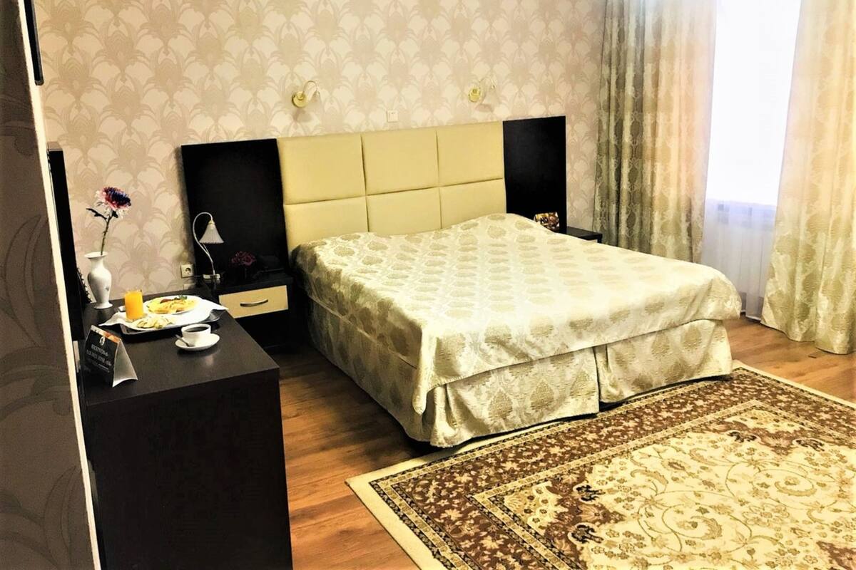 A hotel room with a bed, bedside tables, a desk with a lamp, a vase with flowers, and a rug.